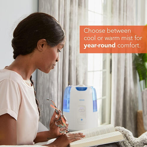 A lady reading in a room with soothing mist released from Vicks Dual Comfort Cool and Warm Mist Humidifier