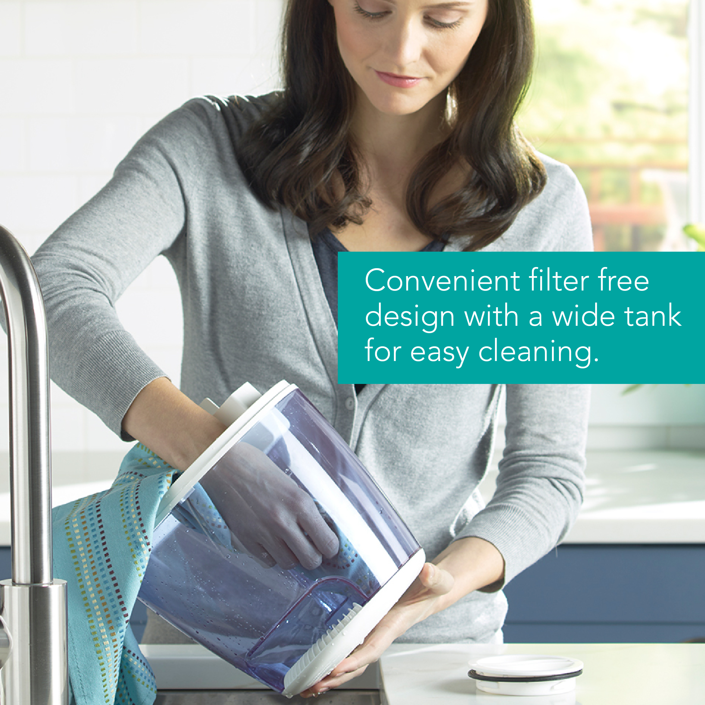A lady cleaning the Vicks humidifier tank with a cleaning cloth through the wide opening of the tank easily with text Convenient filter free design with a wide tank for easy cleaning